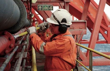 Arbetare i orange skyddskläder med hjälm på offshoreplattform, Reál Marine industrimiljö