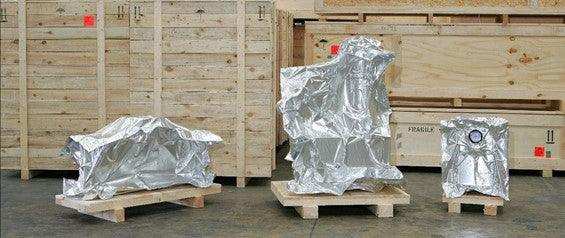 Maskiner inneslutna i aluminiumskydd på pallar framför träemballage, Reál Marine preservering